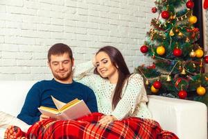 Pretty happy couple in love reads a christmas fairy tail on couch photo