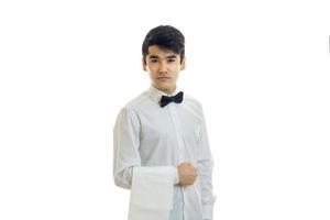 handsome waiter in a white shirt and black bow tie looks right and keeps on hand a towel photo