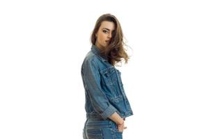 young cute brunette with beautiful hair stands sideways in a jeans suit and looking at camera photo