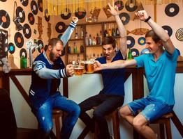 los hombres celebran en el bar y tintinean vasos con cerveza foto