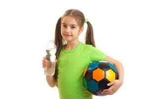 Cute little girl with soccer ball in hands drinks water in bottle photo