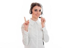 beautiful young girl in headphones and a white shirt looks sideways smiles and shows her finger photo