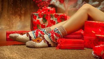 Horizontal photo of sexy female legs in funny socks with a lot of christmas gifts