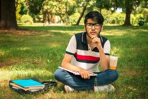 young guy sitting on the grass with books and looks ahead on a summer day photo