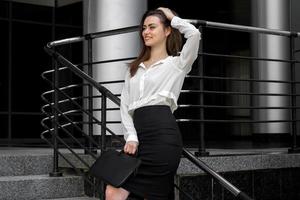 attractive business woman in a white shirt and black skirt stands in the street photo