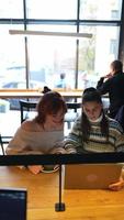 Young women in a cafe talking and using laptop video