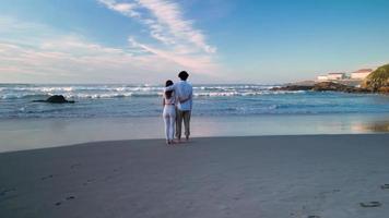 doce casal olha para as ondas na praia de caion paradise na espanha. tiro aéreo drone video