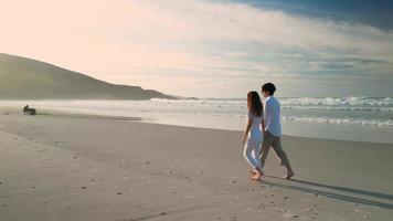 pareja de turistas tomados de la mano mientras caminan en una playa de verano en praia de caion, españa. tiro de seguimiento video