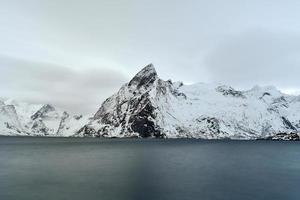 cabaña de pesca en el pico de la montaña hamnoy y lilandstinden en invierno en reine, islas lofoten, noruega. foto