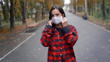 cheerful brunette woman take on a medicine mask on her face at warm autumn day at the park video