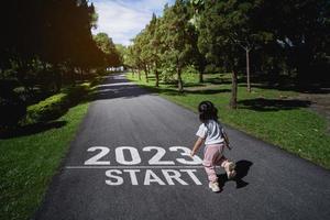Asian baby running start into the new year 2023. Start up of runner woman running on nature race track go to Goal of Success. People running as part of Number 2023. Sport health care. photo