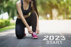 Sport woman runner tie shoelaces start into the new year 2023. Start up of runner woman running on nature race track go to Goal of Success. People running as part of Number 2023. Sport health care. photo