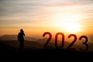fotógrafo parado en la montaña y sesión de fotos, concepto de feliz año nuevo 2023, silueta de éxito con un hermoso fondo de puesta de sol. feliz año nuevo 2023 para banner web y publicidad. foto