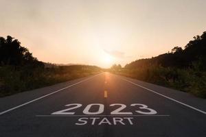 feliz año nuevo 2023,2023 simboliza el comienzo del nuevo año. la carta comienza el nuevo año 2023 en la carretera en la ruta de la naturaleza puesta de sol en la carretera tiene ecología del entorno del árbol o concepto de papel tapiz verde foto