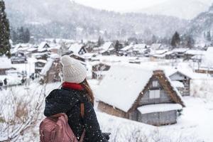 joven viajera mirando el hermoso pueblo patrimonio de la unesco en la nieve en invierno en shirakawa-go, japón foto
