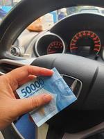 Jakarta, Indonesia on July 2022. A hand is holding a fifty thousand rupiah bill which bends while driving. photo