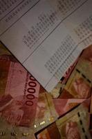 Jakarta, Indonesia on July 2022. A savings book on top of several hundred thousand rupiah bills scattered around. photo