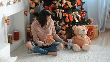 bela morena sentada perto de uma árvore de natal com brinquedos e sorrisos em casa video