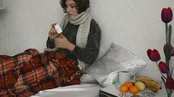 une femme malade est allongée dans son lit avec des pilules sous une couverture à la maison video