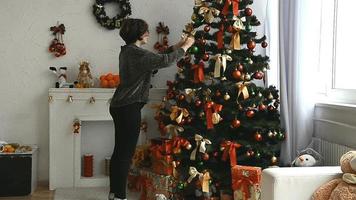 mujer joven con pelo corto decora el árbol de navidad en casa video
