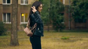 encantadora joven morena latina con chaqueta de cuero camina por la calle y posa ante la cámara video