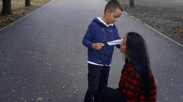 young preschooler boy put a medical mask on his mothers face at the park outdoors