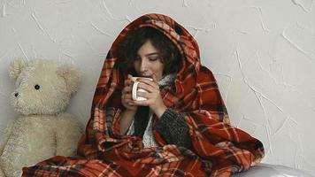 a sick woman drinking a hot drink under a blanket at home video