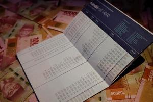 Jakarta, Indonesia in December 2022. A bank Mandiri savings book on several hundred thousand rupiah notes scattered around. photo