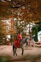 montando a caballo, caminando en un bosque de otoño, una mujer montando a caballo con un largo vestido rojo con los pies descalzos. foto