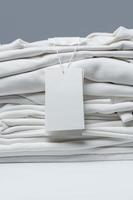 Stack of new white clothes with a blank garment tag photo