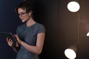 Businesswoman using wireless earbuds and tablet pc during late night work photo