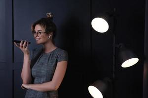 Businesswoman using wireless earbuds and smartphone during late night work photo