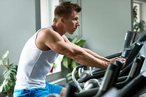 Young muscular man on exercise bike in gym photo