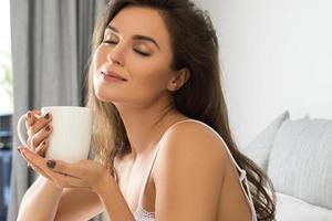 Beautiful woman drinking coffee or tea in bedroom photo