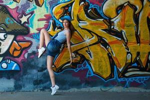 Girl in denim overalls posing against wall with graffiti photo