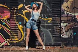 Girl in denim overalls posing against wall with graffiti photo