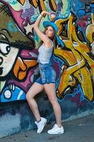 chica en overoles de mezclilla posando contra la pared con graffiti foto