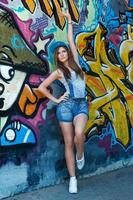 Girl in denim overalls posing against wall with graffiti photo