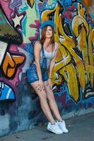 chica en overoles de mezclilla posando contra la pared con graffiti foto