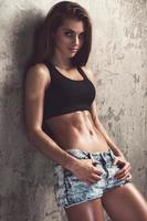 Fitness girl wearing jeans shorts against concrete wall photo