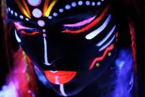 Woman in image of Native American with neon makeup, which made of fluorescent paint in ultraviolet light. photo