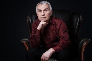 Portrait of serious senior man in armchair photo