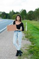 Hitchhiker on the road is holding a blank cardboard sign photo