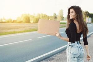 Hitchhiker on the road is holding a blank cardboard sign photo