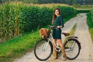 la mujer va en bicicleta por la carretera rural en el maizal foto