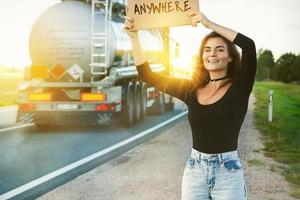 Woman on the road is holding cardboard sign with word ANYWHERE photo