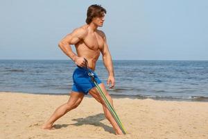 Guy working out with rubber band on the beach photo