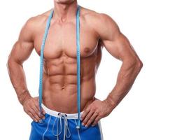 Muscular man with measuring tape over white background photo
