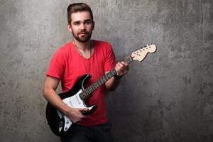 Guy with electric guitar beside concrete wall photo