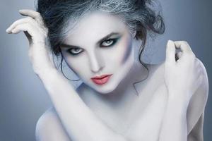 Woman in white body-art in creative image of winter, snow queen, or another sad or evil character photo